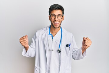 Young handsome man wearing doctor uniform and stethoscope celebrating surprised and amazed for success with arms raised and open eyes. winner concept.