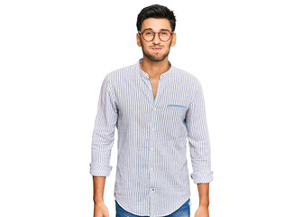 Young handsome man wearing casual clothes and glasses puffing cheeks with funny face. mouth...