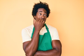 Handsome african american man with afro hair wearing waiter apron looking stressed and nervous with hands on mouth biting nails. anxiety problem.