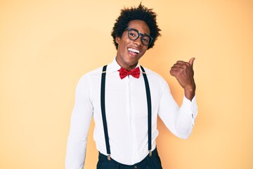 Handsome african american man with afro hair wearing hipster elegant look smiling with happy face looking and pointing to the side with thumb up.