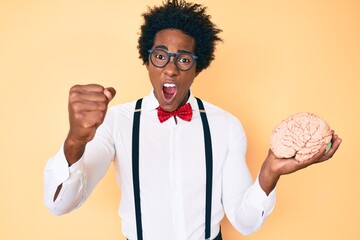 Handsome african american nerd man with afro hair holding brain annoyed and frustrated shouting...