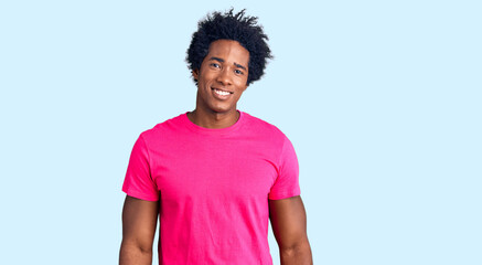 Handsome african american man with afro hair wearing casual pink tshirt looking positive and happy standing and smiling with a confident smile showing teeth