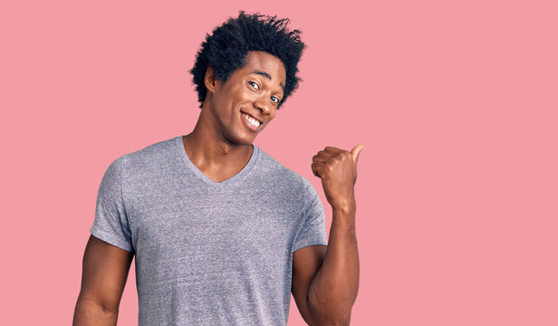 Handsome african american man with afro hair wearing casual clothes smiling with happy face looking and pointing to the side with thumb up.