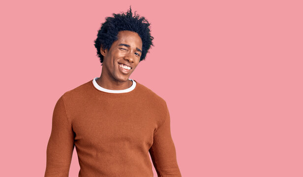 Handsome african american man with afro hair wearing casual clothes winking looking at the camera with sexy expression, cheerful and happy face.