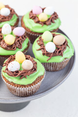 Carrot cupcakes with cream cheese frosting and Easter chocolate eggs, on gray cake stand, vertical