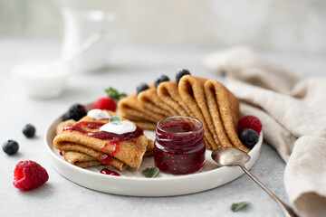 thin sweet pancakes with fresh berries and jam on a gray plate