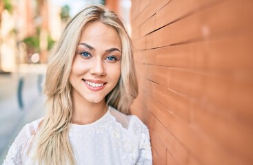 Young caucasian girl smiling happy leaning on the wall at street of city.