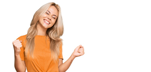Naklejka na ściany i meble Young blonde girl wearing casual clothes very happy and excited doing winner gesture with arms raised, smiling and screaming for success. celebration concept.