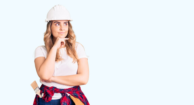 Young caucasian woman wearing security helmet with hand on chin thinking about question, pensive expression. smiling with thoughtful face. doubt concept.
