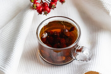 Fruit tea made from berries and rosehip fruits in a transparent glass mug. Hot drink like fresh compote on a white towel