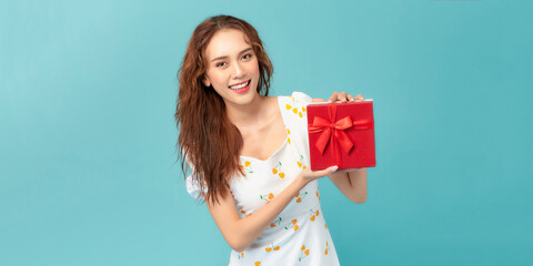 Portrait of a happy smiling girl in dress holding present box isolated over blue background