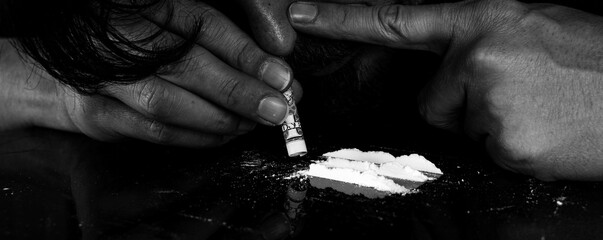 Drug addict man snorting cocaine powder with rolled dollar banknote. Narcotics concept. Dramatic monochrome, black and white photo. Close-up macro shot. Panoramic shot. Panorama banner. - obrazy, fototapety, plakaty