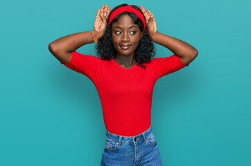 Beautiful african young woman wearing casual clothes doing bunny ears gesture with hands palms looking cynical and skeptical. easter rabbit concept.