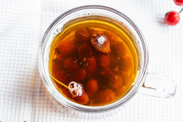 Fruit tea made from berries and rosehip fruits in a transparent glass mug. Hot drink like fresh compote on a white towel