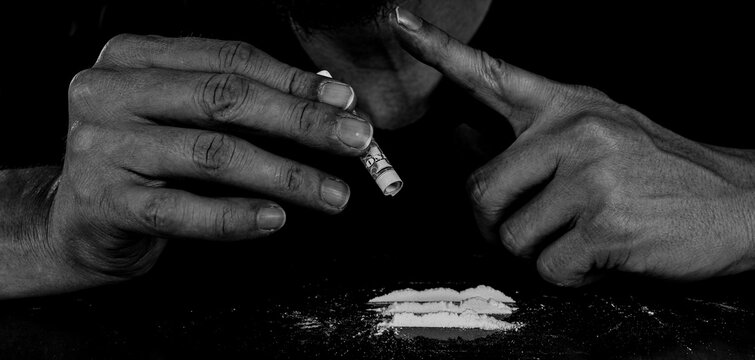 Drug addict man snorting cocaine powder with rolled dollar banknote. Narcotics concept. Dramatic monochrome, black and white photo. Close-up macro shot. Panoramic shot. Panorama banner.