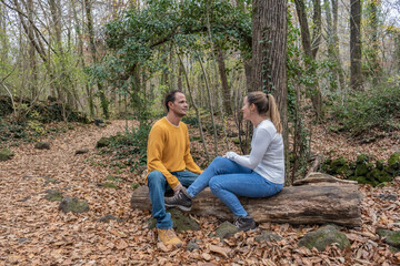 Naklejka na ściany i meble Stylish beautiful young couple talking sitting on woods in beautiful autumn forest landscape.Relationship , love and friends concept lifestyle .