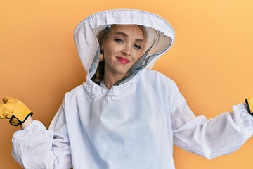 Beautiful blonde caucasian woman wearing protective beekeeper uniform clueless and confused...
