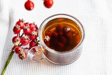 Fruit tea made from berries and rosehip fruits in a transparent glass mug. Hot drink like fresh compote on a white towel