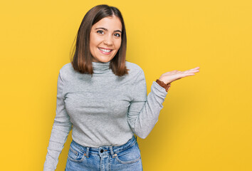 Young beautiful woman wearing casual turtleneck sweater smiling cheerful presenting and pointing with palm of hand looking at the camera.