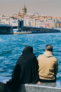 Beautiful vertical shot of a woman and a man sitting on the shore of the ocean looking at waves