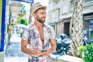 Obraz premium Young hispanic man on vacation smiling happy using smartphone at street of city