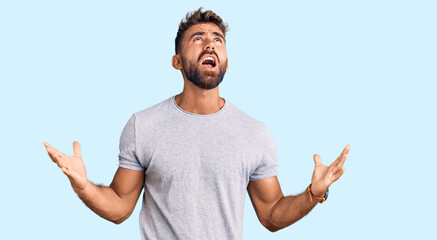 Young hispanic man wearing casual clothes crazy and mad shouting and yelling with aggressive expression and arms raised. frustration concept.