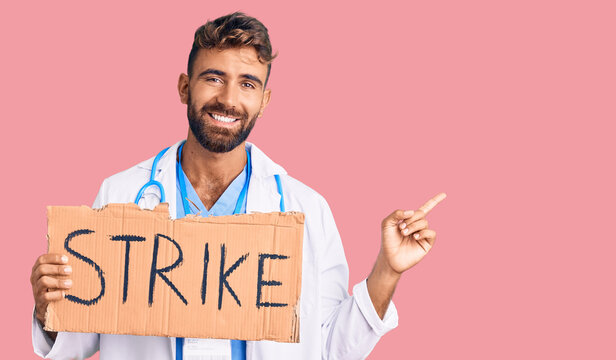Young hispanic man wearing doctor stethoscope holding strike banner smiling happy pointing with hand and finger to the side