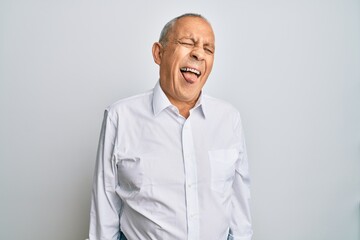 Handsome senior man wearing casual white shirt sticking tongue out happy with funny expression. emotion concept.