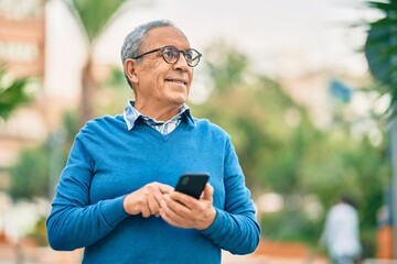 Fototapeta premium Senior grey-haired man smiling happy using smartphone at the city.