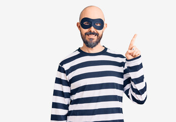 Naklejka premium Young handsome man wearing burglar mask with a big smile on face, pointing with hand finger to the side looking at the camera.
