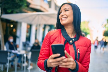 Young latin woman smiling happy using smartphone at the city.