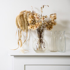 Dried flowers and cereals in a transparent glass decanter stand on a white console in a Scandinavian interior