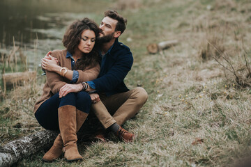 Happy lovers are sitting on the shore of the lake. Young couple is hugging on autumn day outdoors. A bearded man and curly woman in love. Valentine's Day. Concept of love and family.