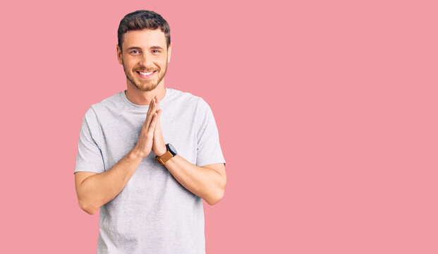 Handsome young man with bear wearing casual tshirt praying with hands together asking for forgiveness smiling confident.