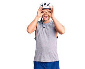 Fototapeta premium Young handsome man wearing bike helmet doing ok gesture like binoculars sticking tongue out, eyes looking through fingers. crazy expression.
