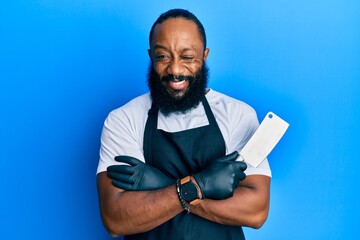 Young african american man wearing professional apron holding knife winking looking at the camera...
