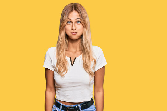 Beautiful blonde young woman wearing casual white tshirt puffing cheeks with funny face. mouth inflated with air, crazy expression.