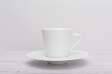 Fototapeta na wymiar Selective focus, white ceramic tea or coffee cup with a saucer on white wooden table against white blurry background. 