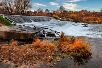 Autumn landscape. Streams of water, shot with long exposure, fall on a man-made dam. Autumn man-made waterfall landscape