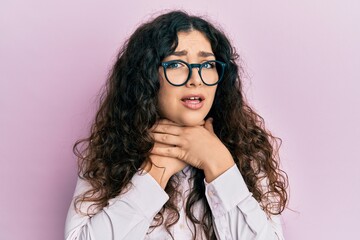 Young brunette woman with curly hair wearing casual clothes and glasses shouting and suffocate...
