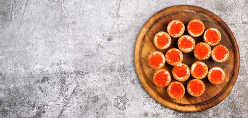 Tartlets with salmon red caviar and feta cheese on a round wooden cutting board on a dark...