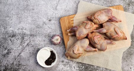 Raw quails on a rectangular cutting wooden board on a dark background. Top view, flat lay