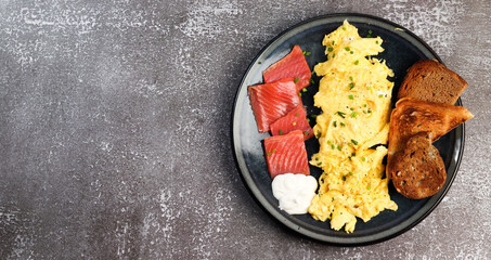 Scrambled eggs with salmon and toast on a round plate on a dark background. Top view, flat lay