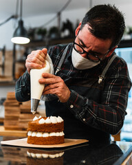 Masked pastry chef filling a cream cake with a piping bag in a hipster bakery