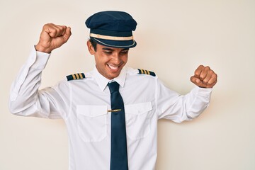 Young hispanic man wearing airplane pilot uniform dancing happy and cheerful, smiling moving casual and confident listening to music