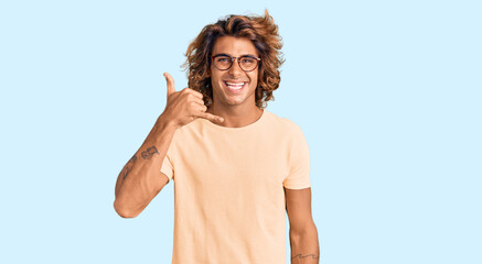 Fototapeta premium Young hispanic man wearing casual clothes and glasses smiling doing phone gesture with hand and fingers like talking on the telephone. communicating concepts.