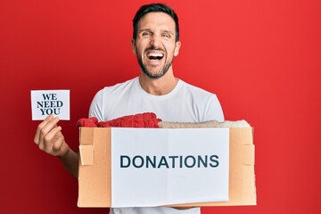 Young handsome man holding donations box and we need you paper smiling and laughing hard out loud because funny crazy joke.