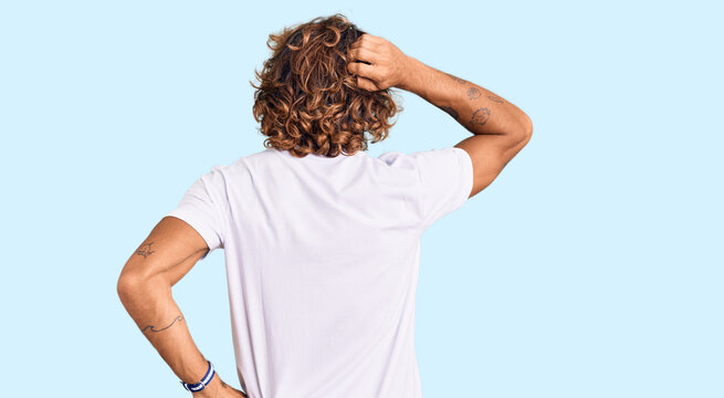 Young hispanic man wearing casual white tshirt backwards thinking about doubt with hand on head