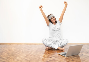 Young woman sitting on the floor with laptop. She is holding hands up and smiling. She looks...