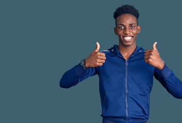 Fototapeta premium Young african american man wearing sportswear success sign doing positive gesture with hand, thumbs up smiling and happy. cheerful expression and winner gesture.